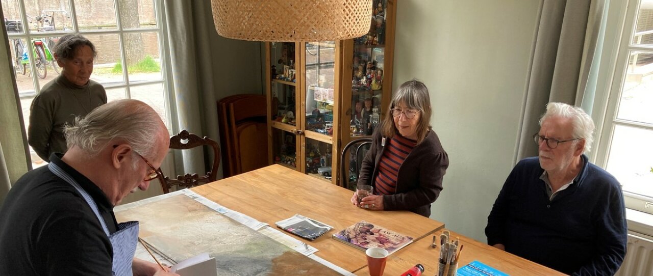 Ouderen zitten aan een tafel in het Huis van de Tijd, een van hen is aan het schilderen, de anderen kijken aandachtig. Publicatie van ZonMw.