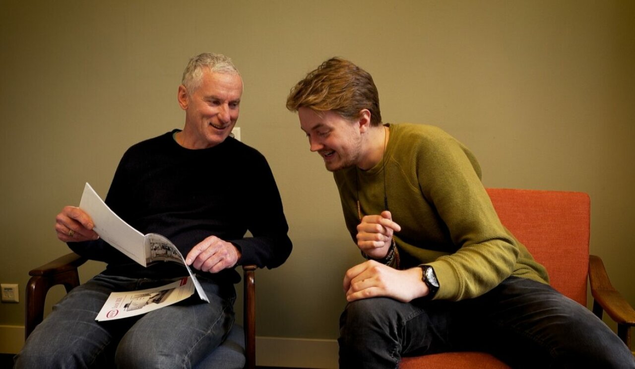 Twee mensen, Joeri en Kayan, zitten op een stoel en lachen om iets. Foto: Joost Honselaar voor Nieuw Wij.