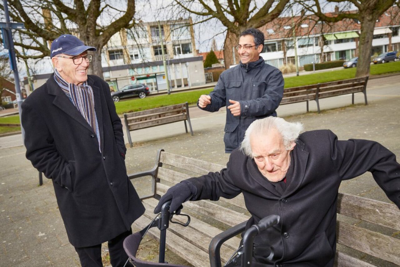 Drie ouderen lachen, een zit op een bankje, twee staan eromheen. Foto van SOL Netwerk voor artikel Sociale Benadering Dementie.